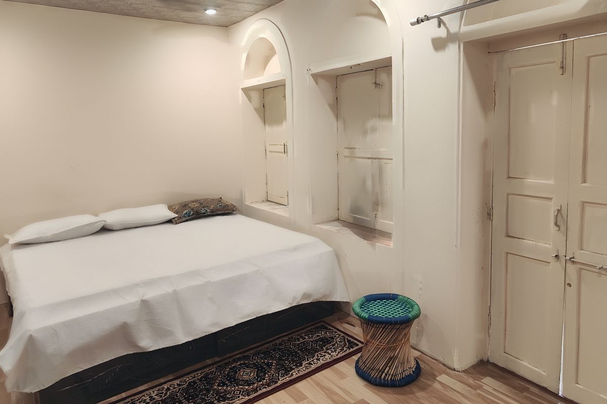 A heritage room at Aghora with arched wall niches, an old panelled door and a woven mudha stool